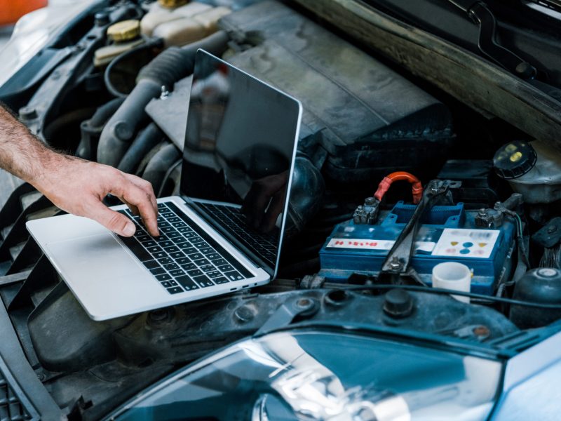 cropped view of car mechanic using laptop with blank screen near car