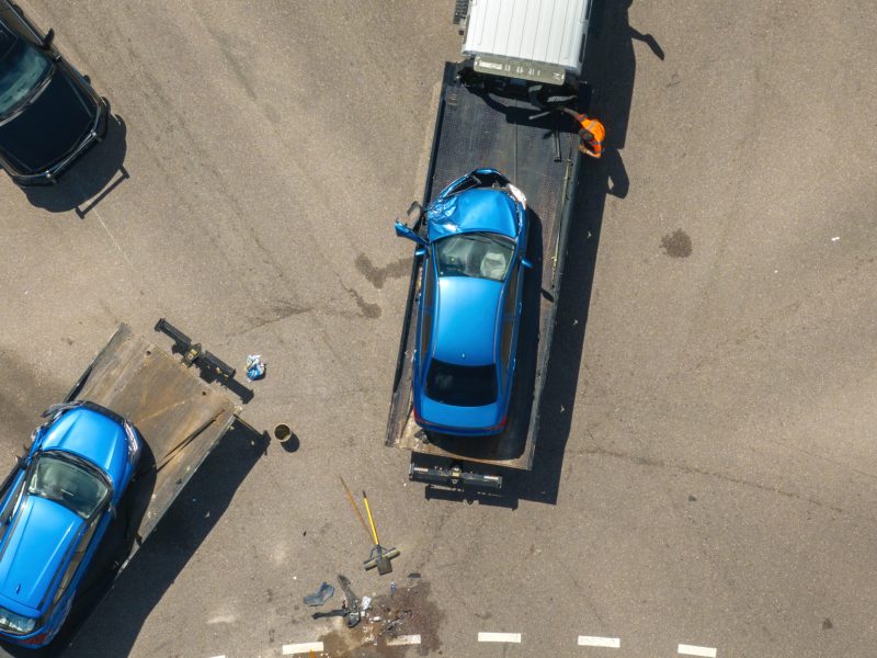Tow truck hauling smashed vehicle on car accident site. Emergency services responding to traffic crash on American street. First responders helping on road in the USA.